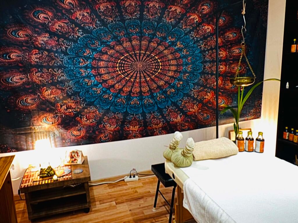 Ájurvédikus kezelőszoba mandala falikárpittal, masszázságy gyógynövényes olajokkal és potali batyukkal — Chandra Ayurveda Budapest